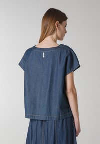 Blå denimskjorte med løs pasform, korte ærmer og rund udskæring. Har synlige sømme og et lille label på bagsiden.