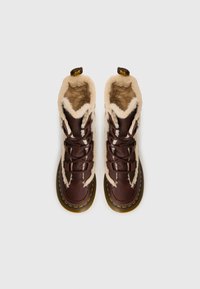 Brune læderstøvler med en fluffy beige foring, der har snørebånd, gule syninger og en rund sål. Set oppefra.