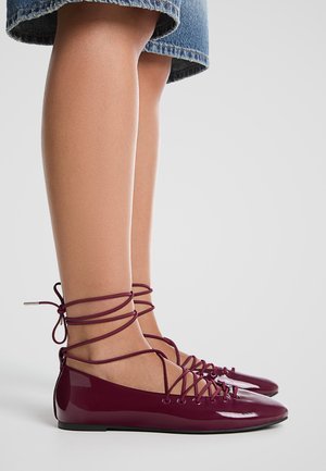 Bordowe baleriny z lakierowanej skóry z ozdobnym wiązaniem, niskim profilem i szpiczastym noskiem. Gładka tekstura i minimalistyczny styl.