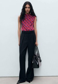 Red and purple checkered sleeveless top paired with high-waisted black trousers and a black handbag. Points shoes complete the look.