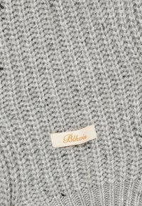 Tejido de punto gris claro con una pequeña etiqueta beige cosida, que presenta el nombre de la marca "Blkvis" en texto cursiva naranja.