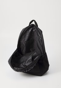 Sac à dos noir avec une ouverture zippée, poche latérale en mesh et doublure intérieure de marque. Extérieur lisse avec un design simple et moderne.