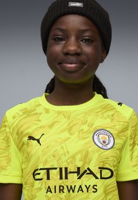 Maglia neon gialla del Manchester City con motivo astratto, logo Puma nero, testo "ETIHAD AIRWAYS" in nero e badge del team ricamato.