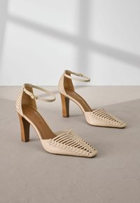 Beige korkokenkiä, joissa on avonainen kudontasuunnittelu ja nilkkahihnat, teräväkärkiset ja teksturoitu puukorko.