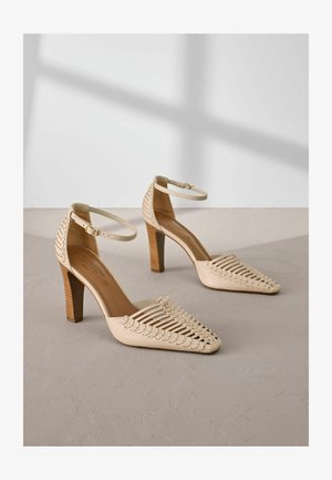 Chaussures à talons hauts beiges avec un design en tissage ouvert et des brides au niveau de la cheville, dotées d'un bout pointu et d'un talon en bois texturé.