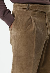 Bruine ribfluwelen broek met duidelijke verticale groeven, een nauwsluitende pasvorm, zijzakken en een riem met een metalen gesp.