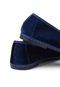 Zapatos de terciopelo azul marino sin cordones con tacón bajo, con una superficie texturizada, costuras a contraste y suela negra flexible.