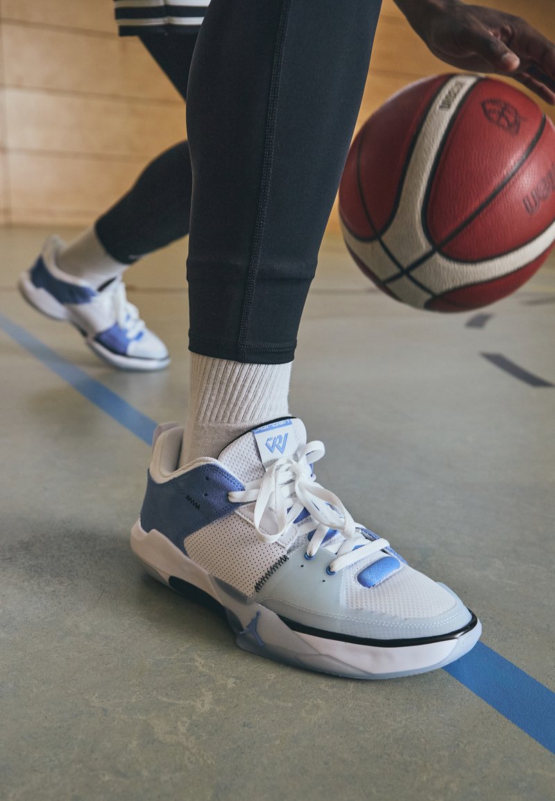 Baltas un gaiši zils basketbola apavu pāris ar sietiņa un zamšādas tekstūru, ar auklām, logotipu uz mēles un elegantu profilu.