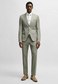 Completo verde chiaro con rever a punta, due tasche frontali e chiusura con un bottone. Abbinato a una camicia bianca e mocassini beige.