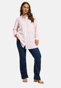 Camicia button-down rosa chiaro con motivo a occhio di pernice, maniche lunghe e orlo curvo, abbinata a jeans blu scuro e sandali con tacco beige.