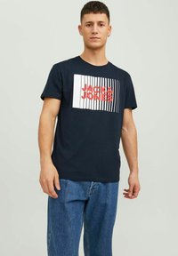 Tricou din bumbac de culoare albastru marin, cu un imprimeu grafic ce prezintă "JACK & JONES" în dungi roșii și albe. Croială standard, cu mâneci scurte.