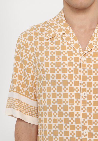Chemise à manches courtes en tissu léger, avec un motif géométrique jaune et crème, dotée d'un col en V et de boutons sur le devant.