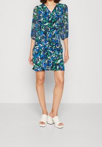 Vestido floral con estampado azul y verde, mangas transparentes y escote en V. Combinado con sandalias blancas de plataforma, puntera abierta y tira ancha.