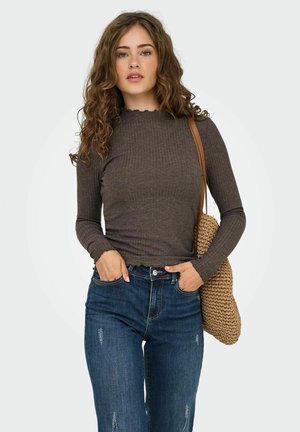 Maglietta marrone a maniche lunghe con coste e polsini a scallop, abbinata a jeans blu strappati e una borsa a spalla in maglia marrone.