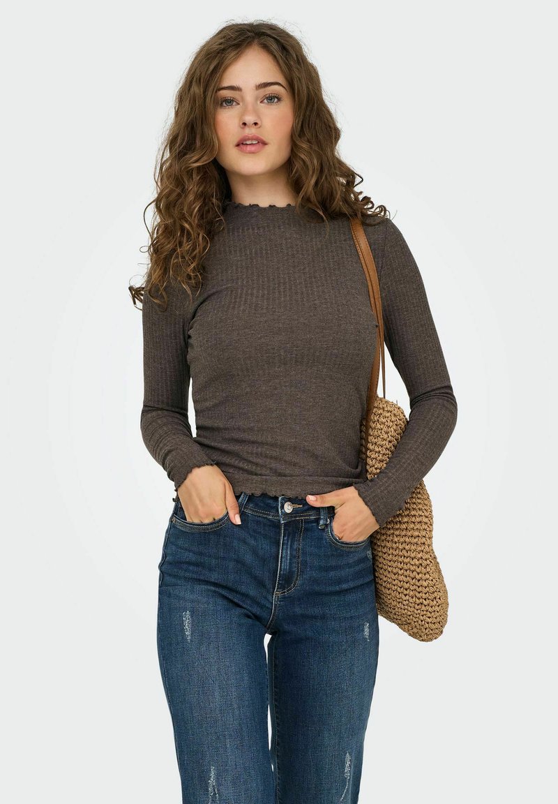 Haut marron à manches longues à côtes avec des poignets à volants, associé à un jean bleu déchiré et un sac en tricot marron porté sur l'épaule.