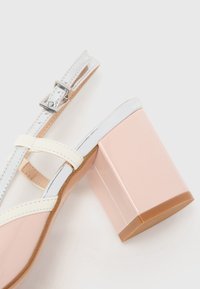 Sandal con tacco rosa dal texture lucido, con cinturini bianchi, dettagli argentati e tacco a blocco spesso. Cinturino alla caviglia regolabile per una migliore vestibilità.