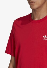Röd bomull T-shirt med korta ärmar, rundad halsringning och en vit Adidas-logotyp på vänster bröst. Slät textur.