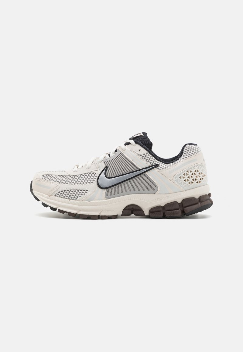 Baskets de running Nike blanches et grises avec semelle noire, panneaux en mesh et logo swoosh noir sur le côté, présentées en profil latéral.