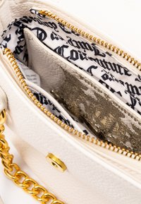 Borsa a tracolla in pelle bianca texturizzata con hardware dorato e catena. L'interno presenta una fodera a motivo con un vano con zip.