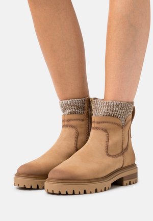 Tan ankle boots with a smooth leather upper and textured knit cuff, featuring a side zipper and a rugged rubber sole.