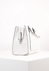 Sac à main en cuir blanc avec bordure noire, forme structurée, fermeture à rabat et poche latérale. Texture lisse avec des accents matériels minimaux.