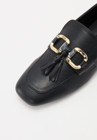 Svart lær loafer med firkantet tå, gullfarget hardware og dekorative kvaster, med en glatt tekstur og slank design.