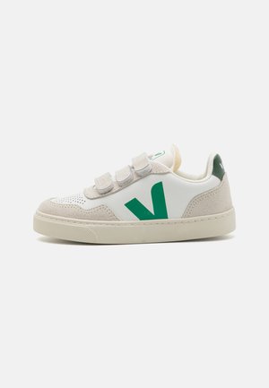 Zapatilla blanca con acentos verdes, material de ante y cuero, correas de gancho y bucle, textura perforada y un diseño de punta redonda.