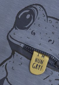 Gray fabric featuring a frog graphic with a zipper. A yellow tag reads "I'M HUNGRY!" contrasting against the blue background.