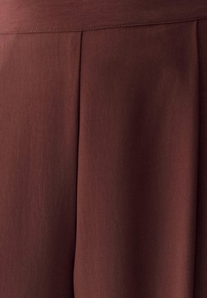 Donkerbruine stof met een verticale naad en plooidetail, die een gladde textuur en subtiele schaduw tonen.