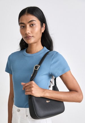 Geantă neagră texturată, cu o formă curbată, accentuată de un logo auriu, asortată cu o cămașă cu mânecă scurtă, cu dungi, de culoare bleu deschis, și pantaloni albi.