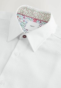 Bela srajca z zapenjanjem na gumbe iz teksturirane tkanine, z ovratnim ovratnikom s cvetličnim in geometrijskim vzorcem ter gumbi bordo barve.