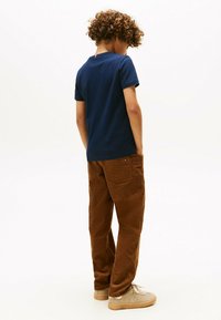 Camiseta de algodón azul marino con escote redondo, combinada con pantalones de pana marrones. Ambos cuentan con bolsillos laterales y se complementan con zapatillas ligeras.