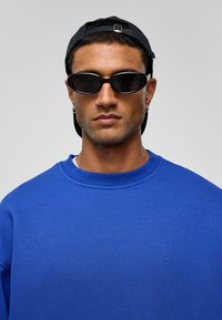 Blauwe sweatshirt met een ronde hals, gecombineerd met stijlvolle zwarte zonnebril. Een zwarte pet achterstevoren voegt contrast toe aan de outfit.