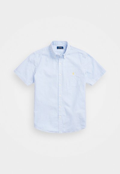 Chemise à manches courtes, à boutons, dans des rayures bleu clair et blanches, dotée d'une poche sur la poitrine gauche et d'un petit logo jaune sur la poche.
