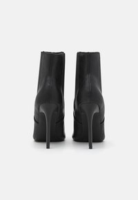 Bottines en cuir noir avec un design élégant, de hauts talons aiguilles et une texture lisse. Construction minimaliste avec des panneaux latéraux élastiques.