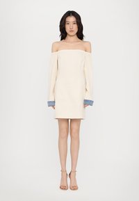 Rochie crem off-the-shoulder din bumbac, cu mâneci lungi și manșete din denim albastru deschis. Siluetă simplă, dreaptă, cu detalii minime.