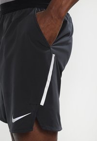 Schwarze Sportshorts mit einer Seitentasche, elastischem Bund und kontrastierendem weißen vertikalen Streifen. Mit kleinem silbernen Nike-Logo.