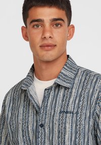 Mønstret button-up skjorte med blå og hvide striber, struktureret stof og et broderet logo på brystet.