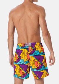 Costumi da bagno colorati con un audace motivo astratto di surfisti e onde in arancione, viola e turchese su uno sfondo giallo.