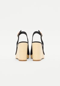 Sandali con zeppa neri e piattaforma intrecciata beige, dotati di cinturini regolabili alla caviglia e accenti metallici rotondi per la chiusura.