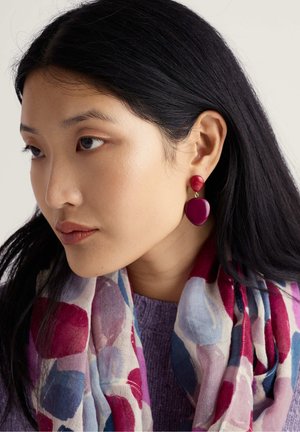 Rdeči in vijolični viseči uhani z sijočim zaključkom. Zgornji delica je okrogla, spodnji pa ima obliko solze. Mehka ruta z abstraktnimi vzorci.