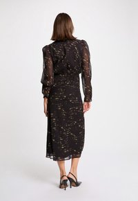 Robe midi noire à manches longues en tissu transparent avec un motif abstrait doré, dotée d'une taille cintrée et d'une jupe fluide.