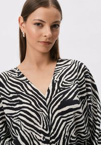 Czarna i biała bluzka w paski zebry z dekoltem w serek i szerokimi rękawami. Teksturowany materiał o płynącym wyglądzie.