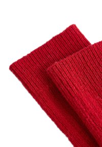 Rode geribbelde tricotstof, zachte textuur, met twee gevouwen delen. De gelijkmatige stiksels benadrukken de dikte en warmte van de stof.