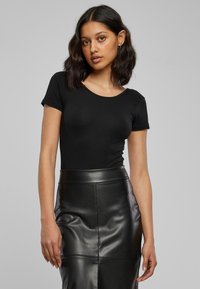 Top nero aderente a maniche corte abbinato a una gonna in pelle nera a vita alta, caratterizzata da una texture liscia e una forma su misura.