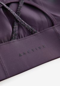 Sujeción deportiva morado con tirantes entrelazados, con un detalle de estampado de leopardo. Tejido texturizado con un acabado suave y logotipo en relieve "ACTIVE".
