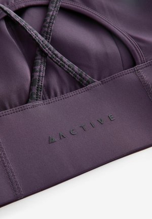 Soutien-gorge de sport violet avec des bretelles croisées, présentant un détail en imprimé léopard. Tissu texturé avec une finition lisse et logo "ACTIVE" en relief.
