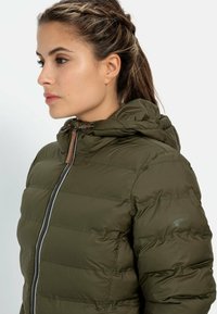 Olive green puffer jacket with a zip front, hood, and quilted design. Features brown leather accents on the zipper. Smooth texture.