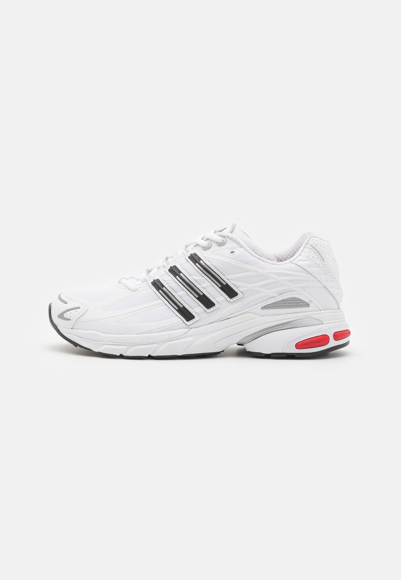 Baskets blanches de sport avec un design à trois bandes noires, semelle texturée, accents gris et détail rouge au talon sur fond uni.