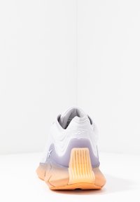 Biały i lawendowy sneaker Reebok widziany od tyłu, z przezroczystym pomarańczowym wspornikiem pięty i teksturowaną podeszwą.